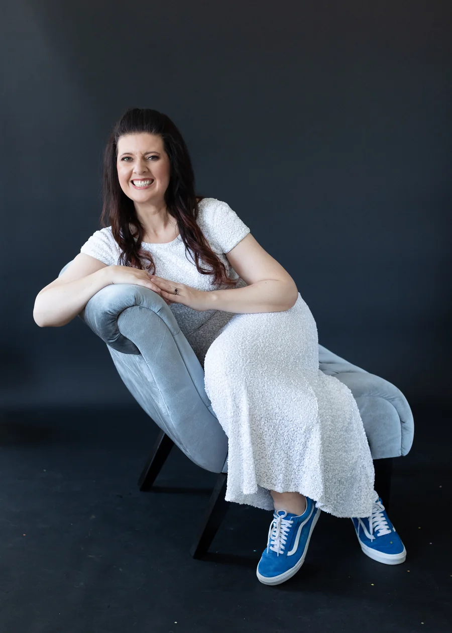 Erica seated in a velvet chair in a sequin gown and blue sneakers, smiling